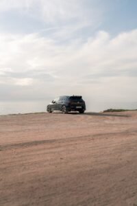 Une voiture garée sur une route calme du désert au bord de la mer, capturant l'aventure en plein air et la tranquillité.