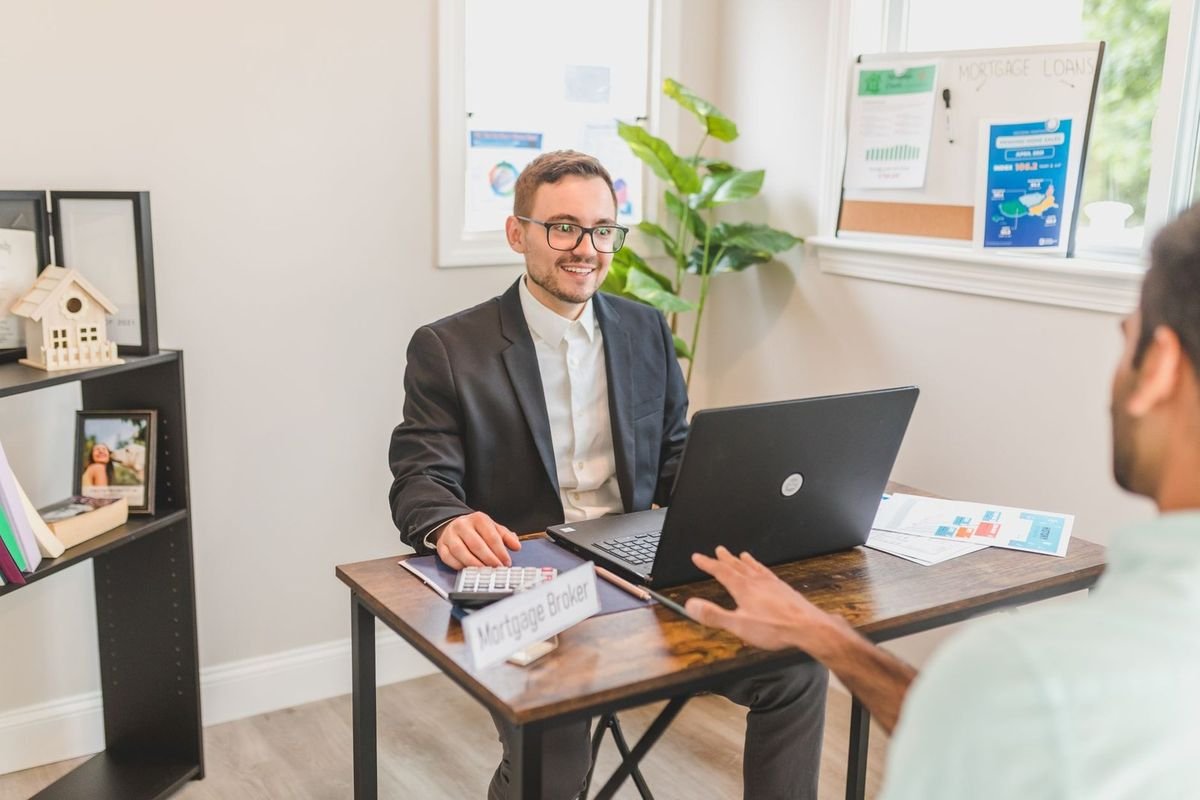 Homme en costume et homme en chemise blanche discutant autour d'un ordinateur portable dans un bureau décoré