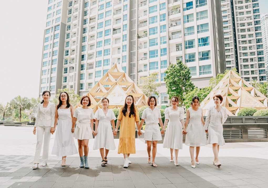 Huit femmes en blanc et une en jaune marchent main dans la main sur un trottoir