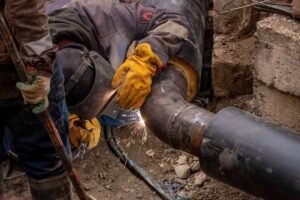 Ouvriers soudant une conduite métallique sous terre, entourés de terre et de roches