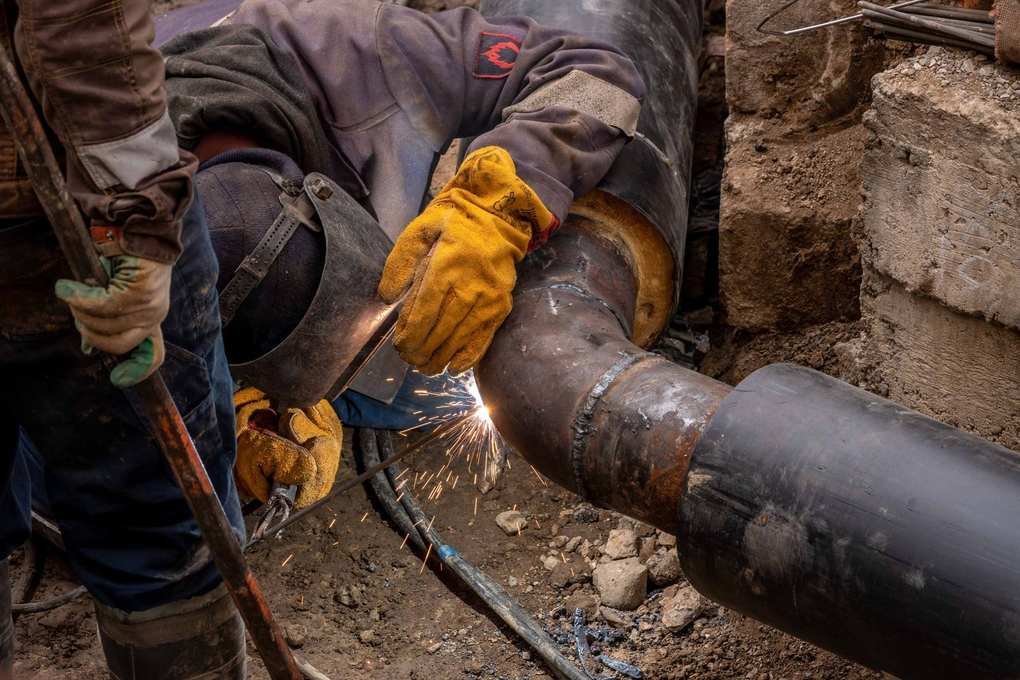 Ouvriers soudant une conduite métallique sous terre, entourés de terre et de roches