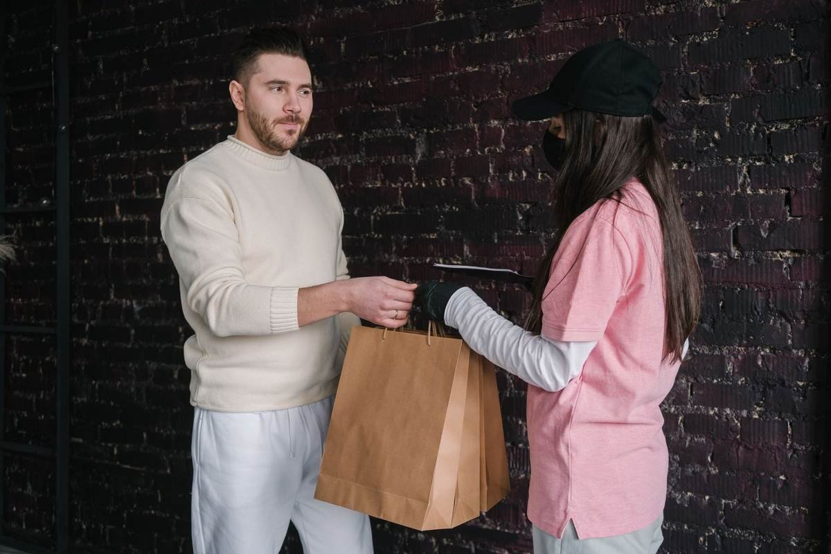 Homme et femme devant un mur de briques échangent un sac brun