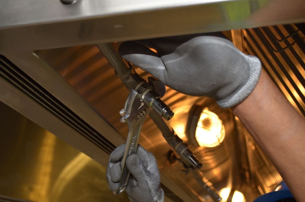 Mains gantées ajustant des tuyaux sous un appareil métallique dans un environnement industriel Mains gantées ajustant des tuyaux sous un appareil métallique dans un environnement industriel