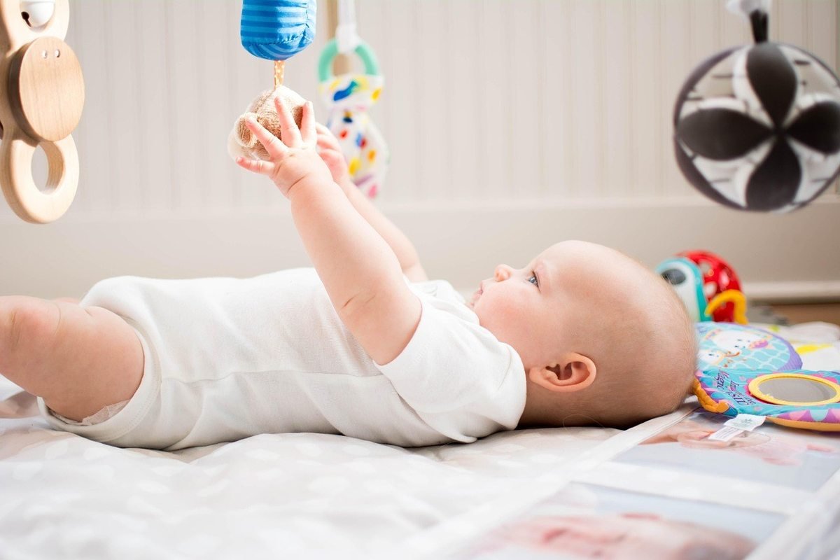 Bébé nu allongé, jouant avec des jouets suspendus, ballon noir et blanc visible Bébé nu allongé, jouant avec des jouets suspendus, ballon noir et blanc visible