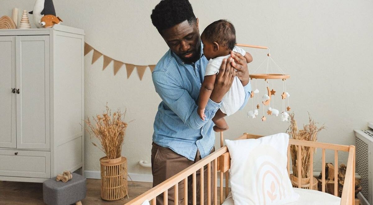 Homme noir portant bébé dans une chambre d'enfant décorée