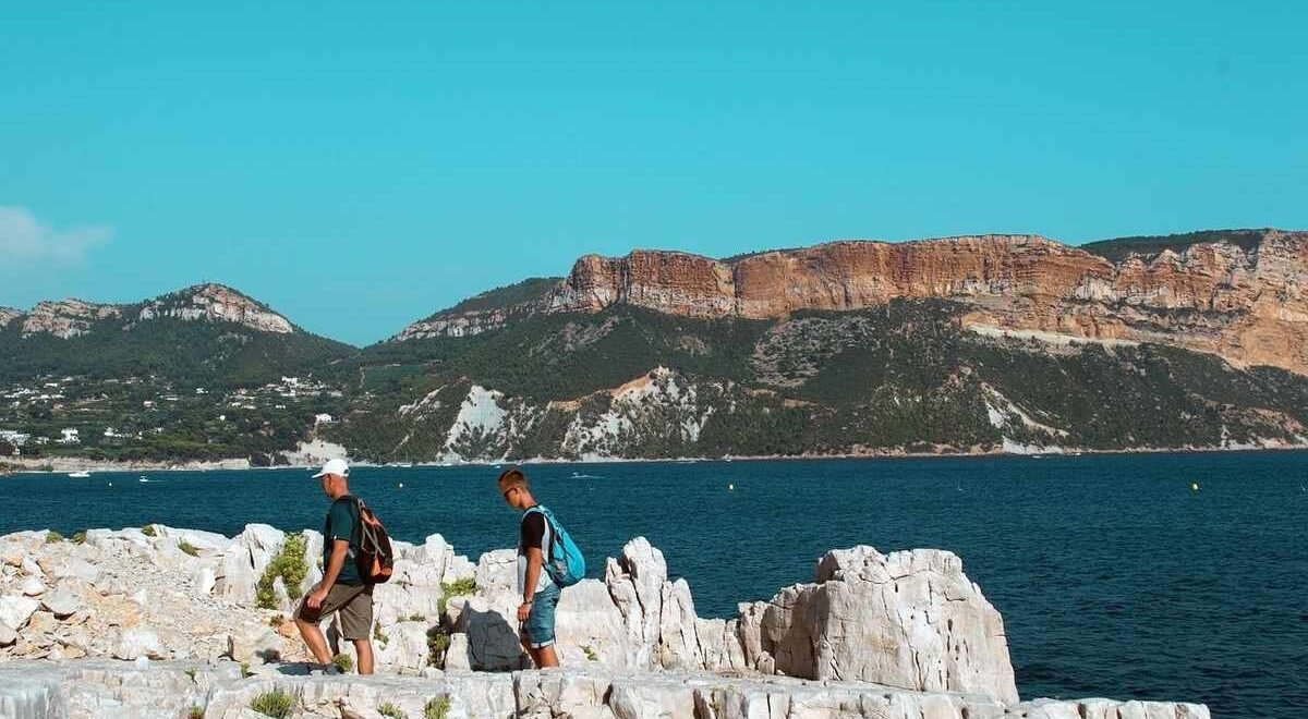 Deux personnes avec sacs à dos marchent sur rochers près de la mer