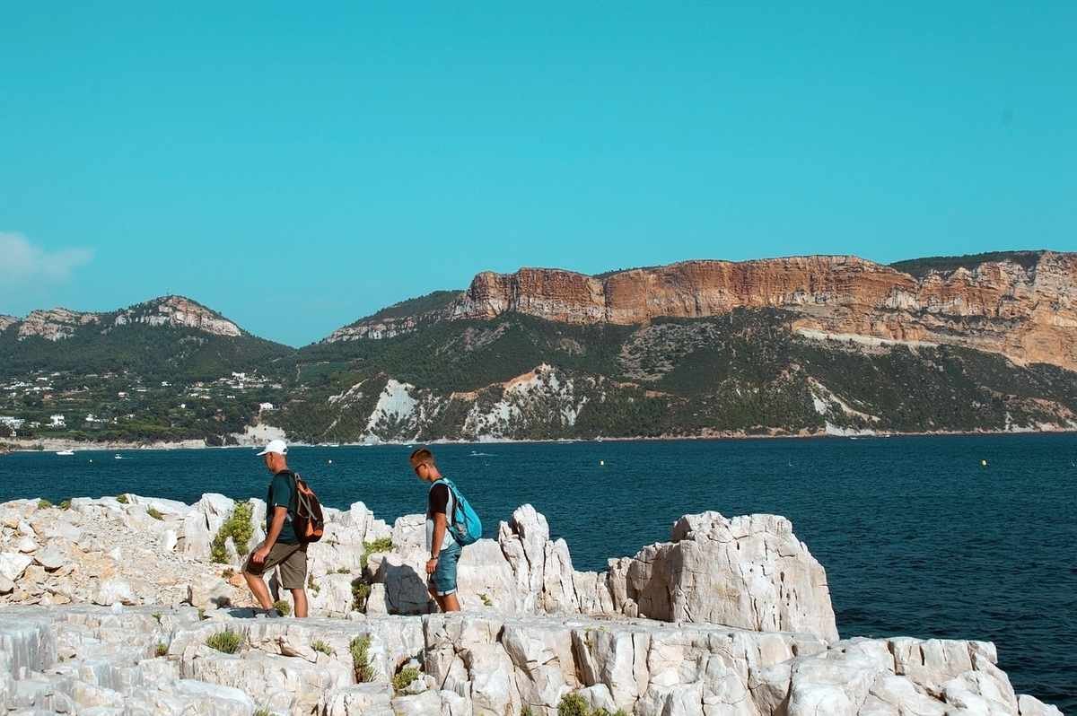 Deux personnes avec sacs à dos marchent sur rochers près de la mer