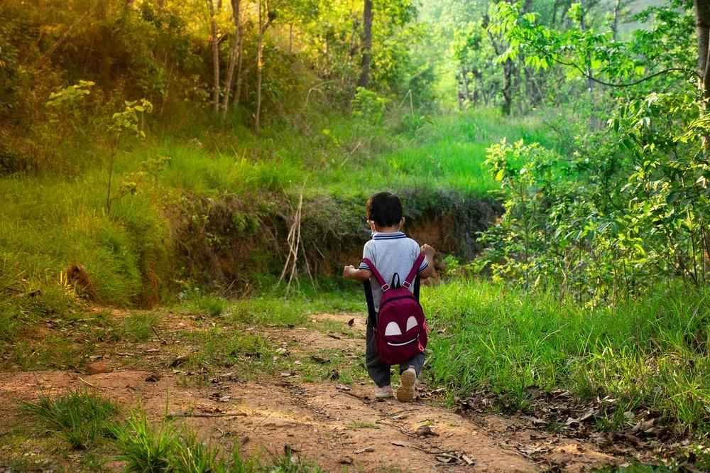 Un petit garçon avec sac à dos marche sur un chemin de terre