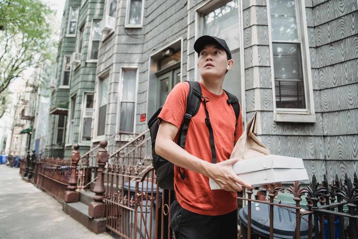 Homme en orange et noir, boîte blanche, rue avec immeubles, capuchon, sac à dos, regard vers le haut