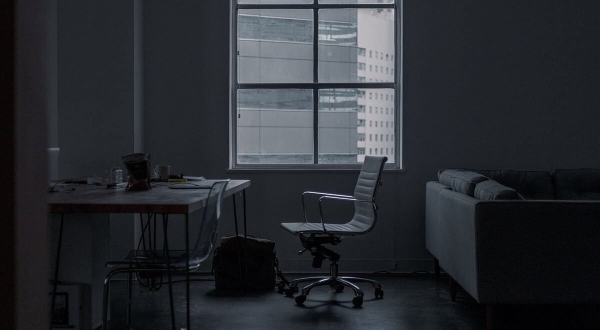 Salle sombre avec bureau, chaise, canapé, fenêtre et sac