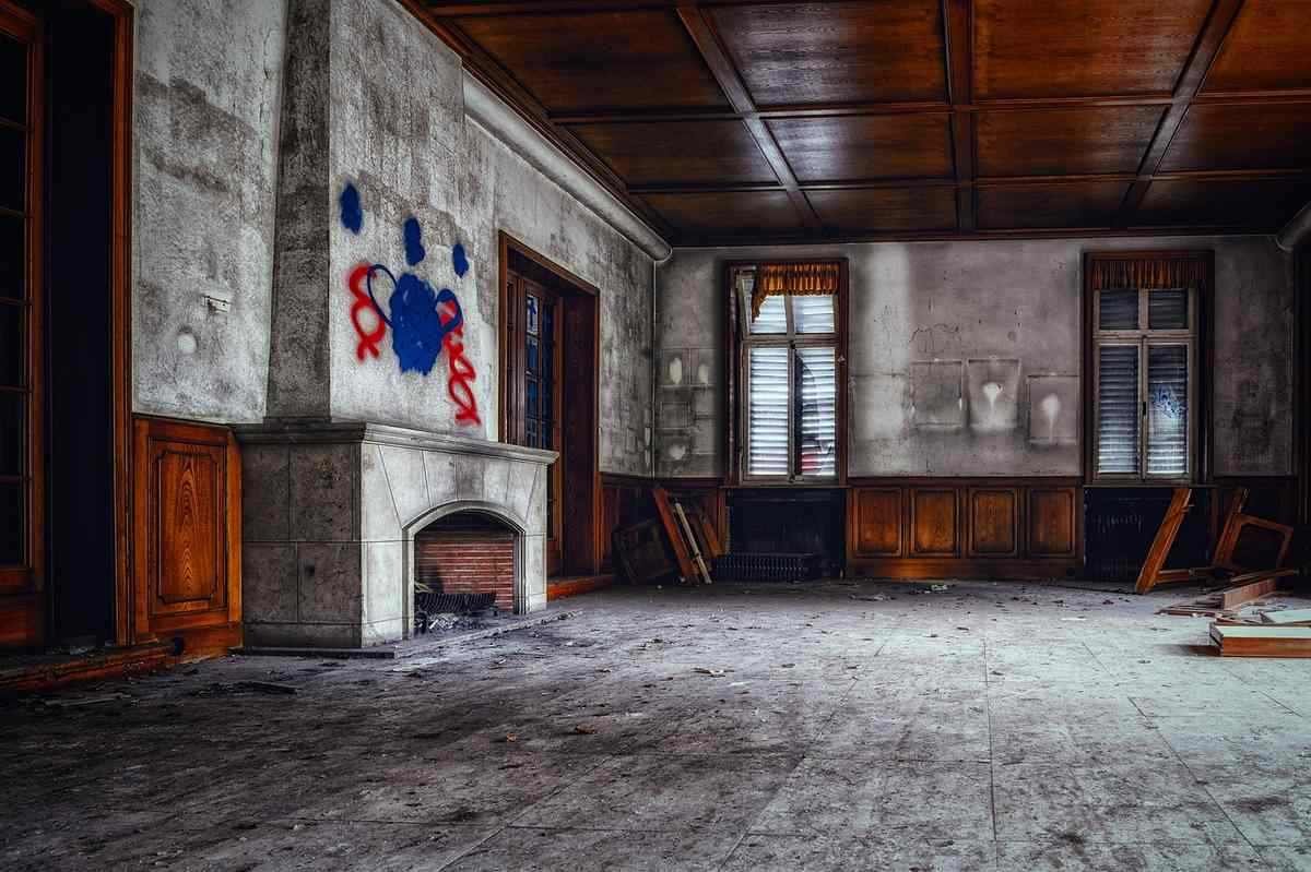 Salle désaffectée avec cheminée, fenêtres et graffiti. Sol poussiéreux, meubles absents Salle désaffectée avec cheminée, fenêtres et graffiti. Sol poussiéreux, meubles absents