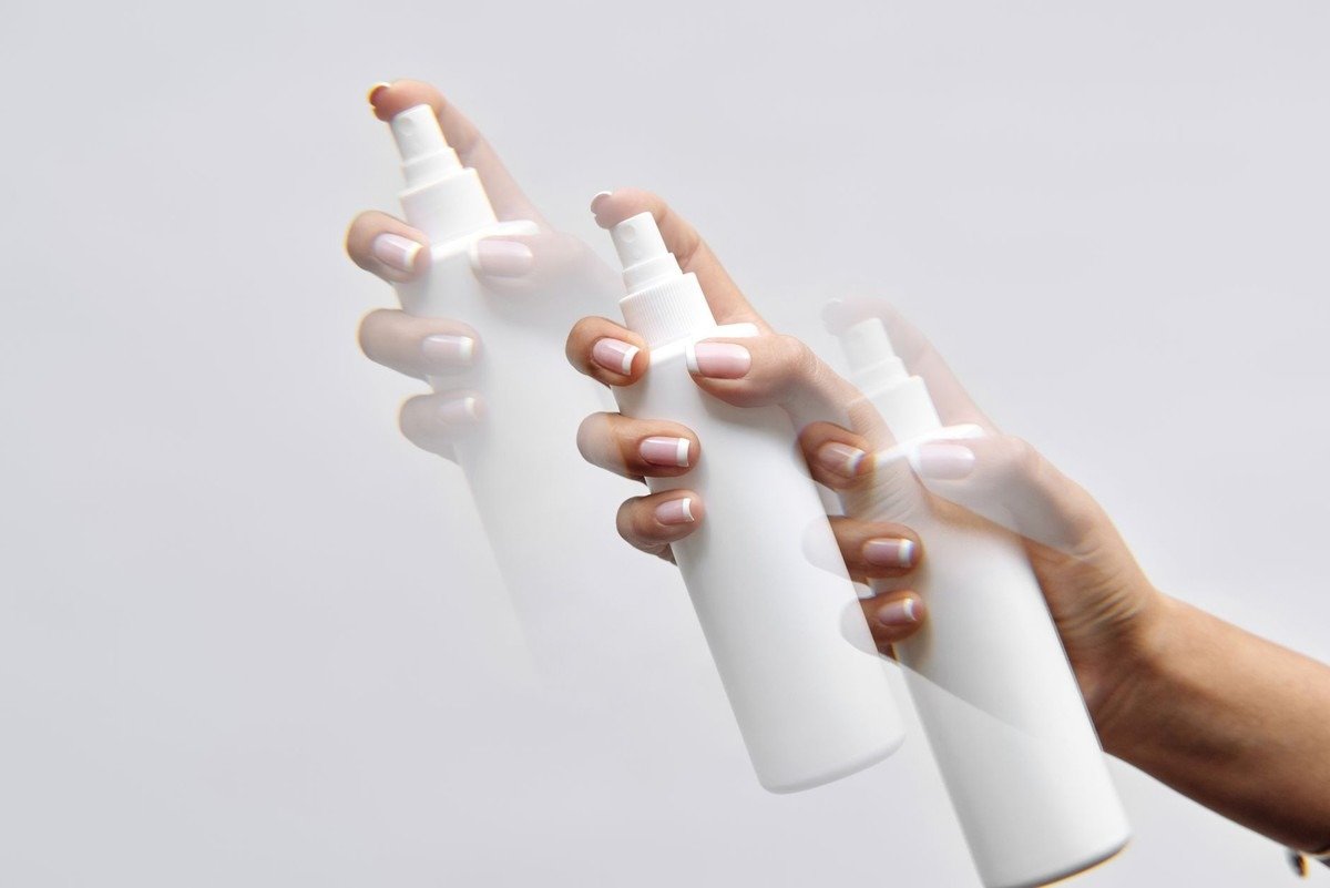 Mains avec flacons de spray en action, fond gris