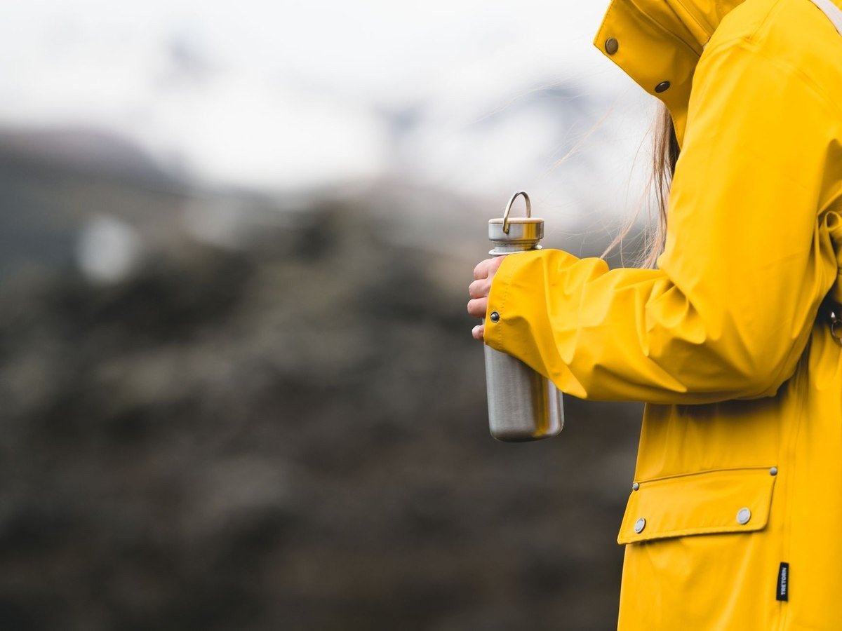 Une personne en veste jaune tient une gourde devant un décor montagneux Une personne en veste jaune tient une gourde devant un décor montagneux