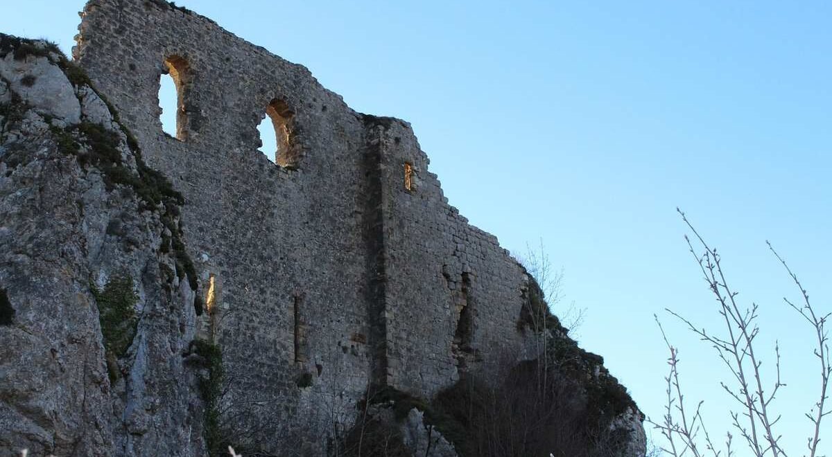 Ruine médiévale sur falaise, fenêtres en arc, ciel bleu, branches nues