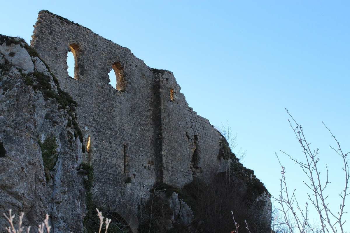 Ruine médiévale sur falaise, fenêtres en arc, ciel bleu, branches nues