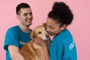 Deux bénévoles caressent un chien joyeux contre un fond rose
