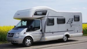 Camping-car de classe moyenne stationné au bord d'une route, paysage agricole avec champ de colza en arrière-plan