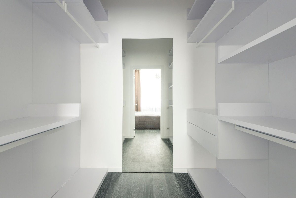 Corridor avec étagères blanches, sol gris, ouverture vers une pièce lumineuse avec lit Corridor avec étagères blanches, sol gris, ouverture vers une pièce lumineuse avec lit