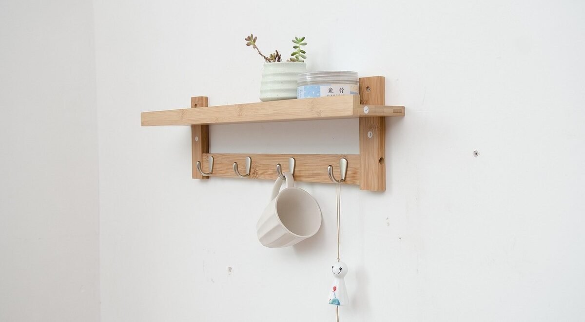 Une étagère en bois fixée au mur, crochets, tasse et petite plante