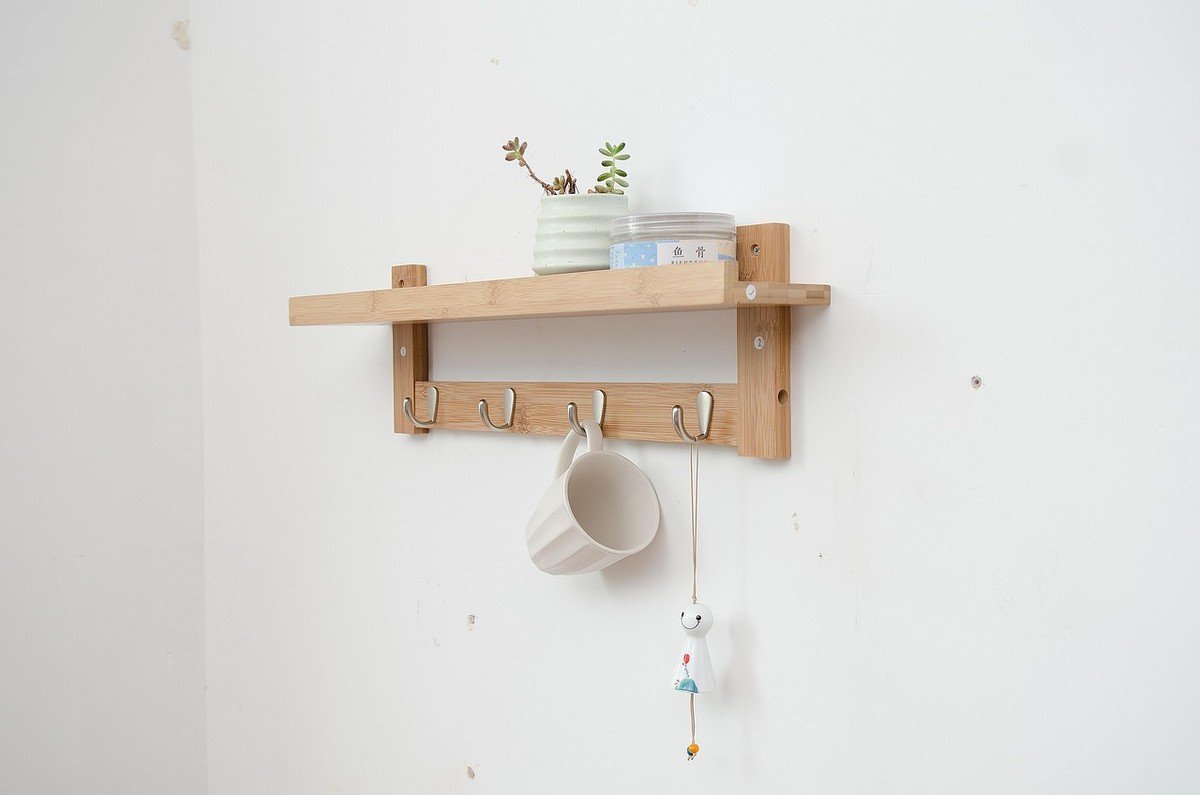 Une étagère en bois fixée au mur, crochets, tasse et petite plante