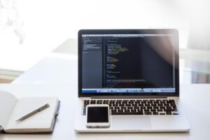 Poste de travail de développeur avec ordinateur affichant du code, smartphone et carnet blanc sur bureau clair