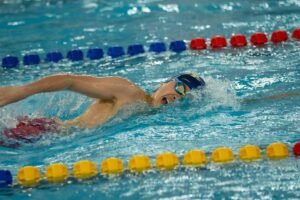 Nageur en pleine course dans une piscine, bras tendu, ligne de flotteurs colorés