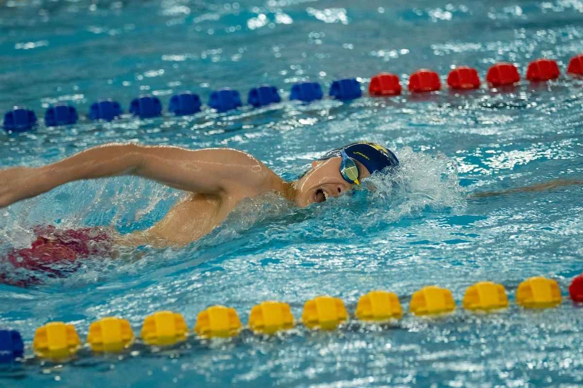 Nageur en pleine course dans une piscine, bras tendu, ligne de flotteurs colorés
