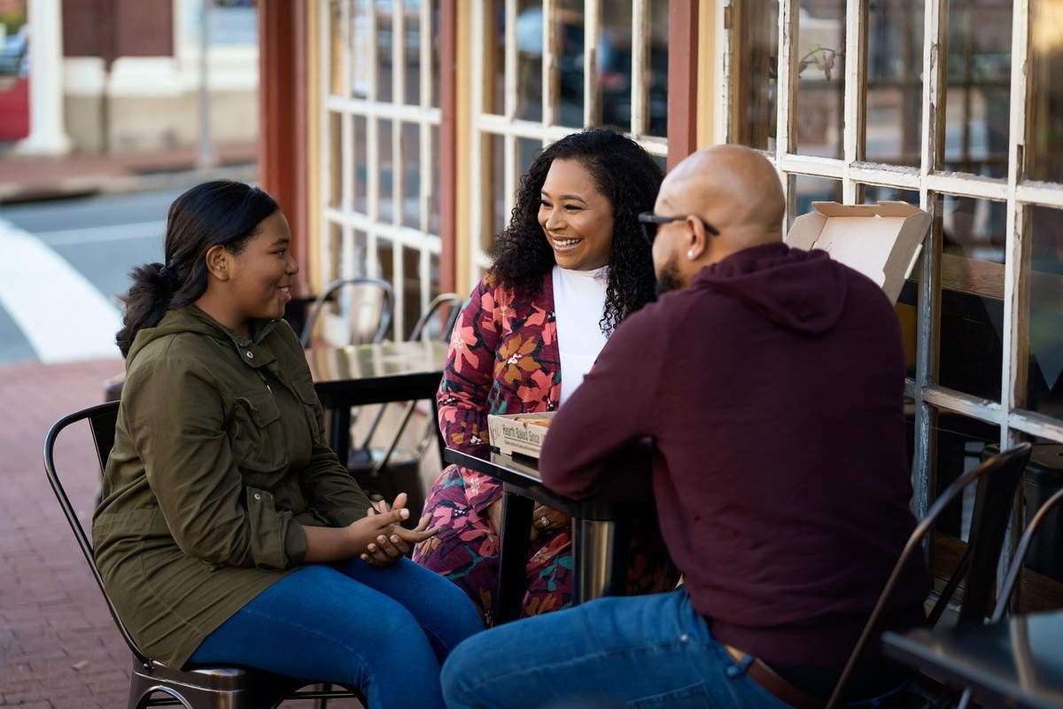 Trois individus en conversation autour d'une table de terrasse dans un café urbain