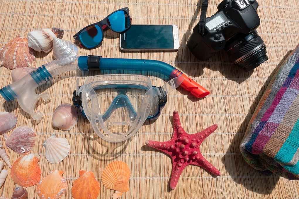 Équipement de plongée, coquillages, étoile de mer, téléphone, appareil photo, serviette sur tapis de paille Équipement de plongée, coquillages, étoile de mer, téléphone, appareil photo, serviette sur tapis de paille