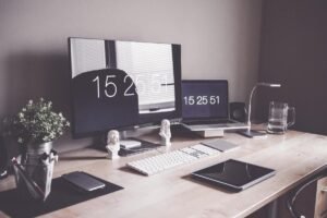 Bureau de travail avec deux écrans affichant l'heure, clavier, plante verte et accessoires