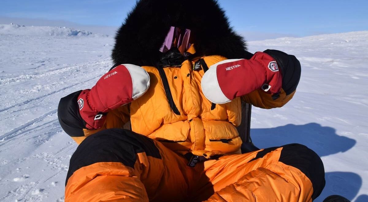 Personne en combinaison orange, gants rouges, casque noir, assis sur traîneau