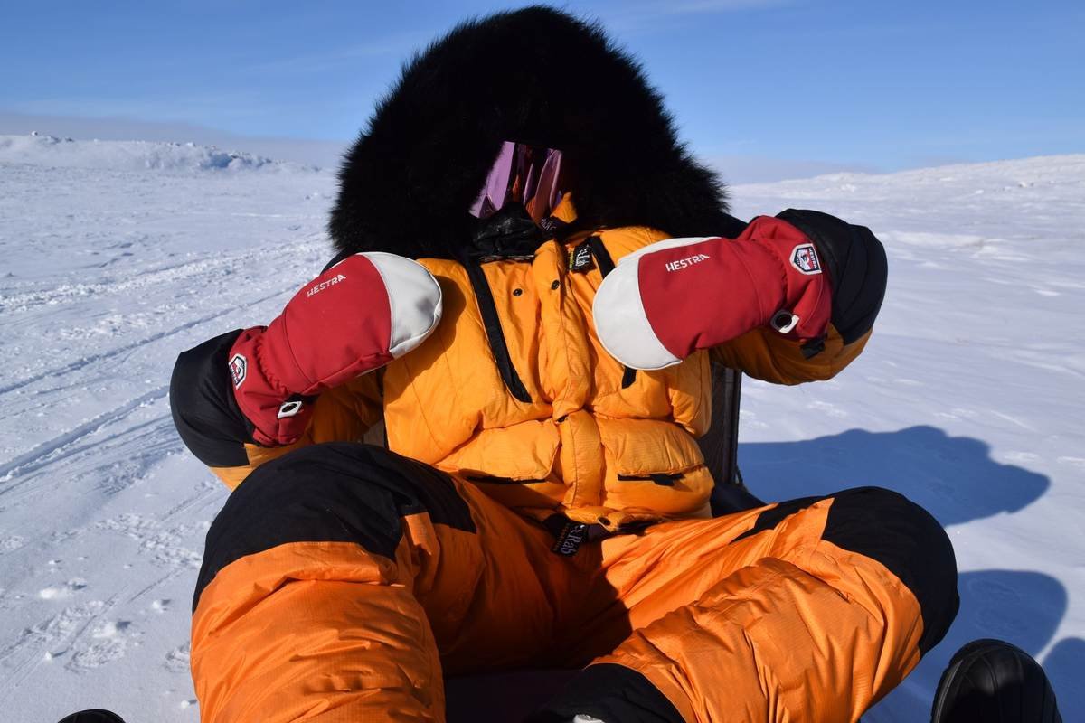Personne en combinaison orange, gants rouges, casque noir, assis sur traîneau