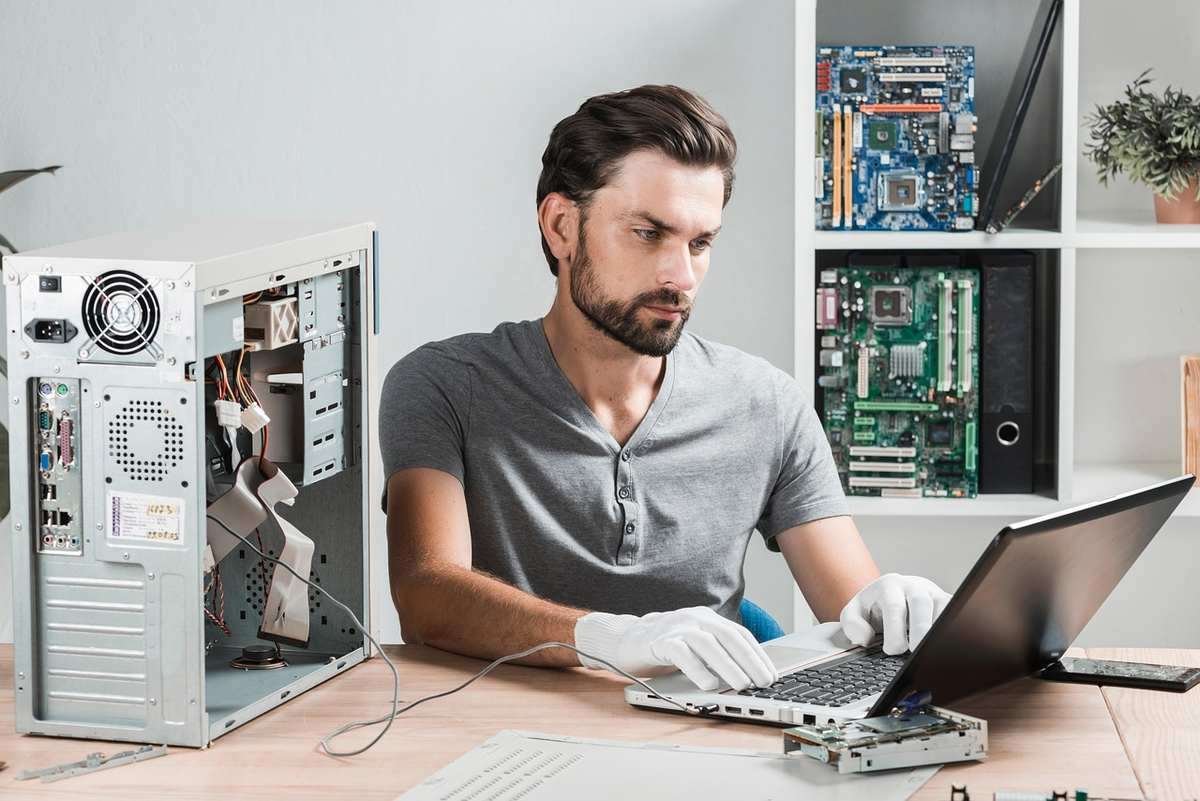 Un technicien en gants travaille sur un ordinateur portable avec un PC ouvert